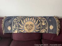 Blanket throw draped over back of couch showing sun and Zodiac design with fringed edges