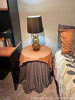 Side view showing round side table with layered fabric covers and lamp on top