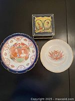 Top-down view of the two plates and tin box on dark surface, showing full designs and borders.