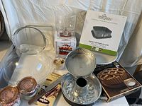 Wide view of assorted cake and pie bakeware pieces including pans, jars, and serving dishes on white table with white backdrop