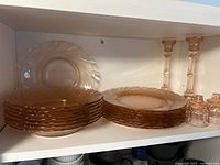 Side view of stacked pink dinner plates and bowls, two larger candle holders, and two smaller matching candle holders on a white shelf.