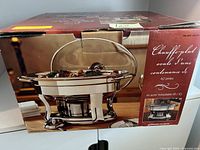 Photo of chafing dish box showing front view of the stainless steel chafing dish with glass lid and a fuel holder underneath.