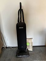 Front view of black Oreck upright vacuum cleaner with power cord wrapped on back and box of Oreck bags placed next to vacuum base