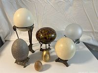 Overview of seven decorative eggs varying in size, color, and stand style on white background