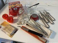 Photo showing caviar serving bowl, seafood forks, egg cooker box, salad tongs, timer, other utensils arranged on clean white table.
