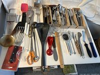 Kitchen utensils and cutlery laid out in drawer organizer showing variety and condition
