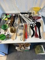Top view of the assorted kitchen utensils laid on a white surface showing various materials and colors.