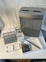 Front view of office supplies lot showing paper shredder, desk organizers, and box of rubber bands on a white surface with a white backdrop.