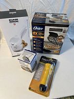 Photo showing Kuhn Rikon potato ricer box, Oster Belgian waffle maker box, meat tenderizer box, and Rayovac flashlight packaging on white surface.