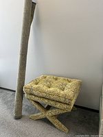 Photo showing the tufted upholstered stool with a crisscross X-shaped base and the roll of matching fabric standing next to it.