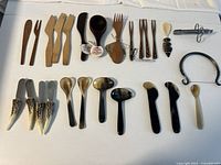 Full display of various serving spoons, forks, wooden and horn utensils arranged on white background.