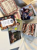 Seven cookbooks arranged on a bed, titles and covers visible