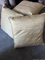 Three light lime green pillows with textured striped fabric and swirl pattern, arranged on carpeted floor.