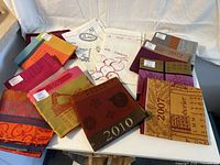 Overview of 10 colorful LeJacquard Francis calendar-themed linens laid out on a table, showing years 2007, 2009, 2010, 2012 among others