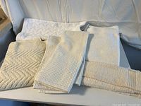 Several bath towels and bath mats folded and laid out on a surface, showing different textures and neutral tones