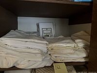 White sheets and pillowcases folded on shelf with a note marked '162'