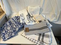 Photo showing the assorted kitchen towels laid out on a white surface, highlighting various patterns including blue floral, utensil prints, stripes, and more.