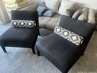 Two black slipper chairs positioned side by side with patterned bolster pillows on each.