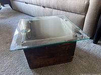 Top view showing clear heavy glass top on wooden base beside sofa.