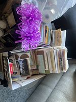 Photo showing boxes filled with greeting cards and decorative purple ribbons on top with assorted gift wrap rolls behind