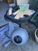 Top view of the grill showing the power cord, skewers, and instruction manual on cooking surface and grill cover under grill.