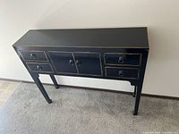 Front view of black wooden hallway table with drawers and cabinet doors.