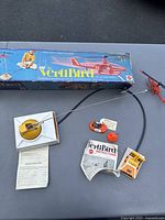 Photo showing the full VertiBird toy set including helicopter, control base, orange buoy, instruction manual and original box with images and logo.