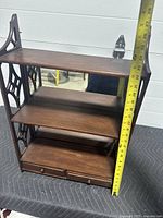 Full view of vintage mahogany shelf showing three wooden shelves and back mirror with lattice sides, and tape measure height at about 22 inches