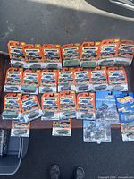 Top-down photo showing 25 vehicles in original blister packaging laid out in multiple rows. Most are Matchbox army vehicles with military themed packaging; two vehicles are Johnny Lightning brand.
