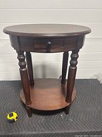 Front view of the oval wooden nightstand showing the drawer, four turned legs, and lower shelf.