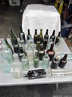 Overview of 31 antique bottles on a table in varying colors including brown, green and clear, with different shapes and patinas.