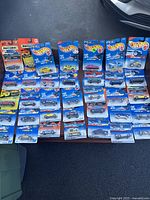 35 new in box Hot Wheels toy cars in original blister pack cards from the 1990s laid out on a surface.