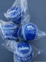 Four blue baseballs sealed in plastic bags with white stitching and printed text.