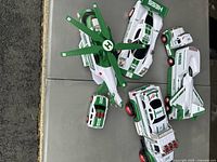 Four Hess toy vehicles arranged on a table showing helicopter, race car, flatbed truck with plane and car carrier truck with cars.