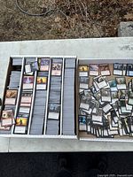 Two cardboard card storage boxes, left filled with cards organized by dividers into five rows, right with loose pile of cards.