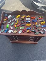 Top-down view of the 50 matchbox cars arranged on a wooden dresser, showing a wide variety of vehicle types and colors.