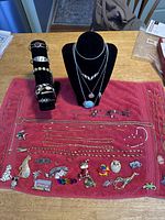 Full view of the costume jewelry laid out on red cloth including necklaces, pins, and bracelets with black display stands in the background.