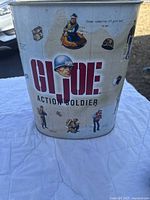 Metal G.I. Joe waste paper basket showing various vintage soldier graphics and G.I. Joe logo, oval shape.