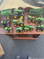 View of all John Deere toy tractors and four wheeler on a wooden dresser.
