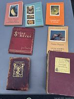 Photo shows one maroon leather bound book of poems by Rudyard Kipling with gold embossing and wear, four softcover National Audubon Society Nature Program books with colorful covers, and one red cloth bound book titled 'Songs of Seven' by Jean Ingelow.