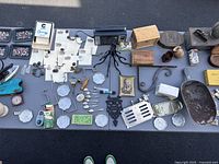 Overview of the table showing multiple vintage items including trivet, silverware, metal kitchen tools, coasters, glass bottles, wooden boxes, and small collectibles.