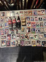 Full table view showing 50 assorted Red Sox baseball cards spread out, two unopened Coca-Cola bottles, three wood plaques with player images, a matchbox, and two plastic figurines.
