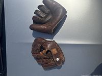 Two vintage leather baseball gloves displayed on a surface under sunlight, showing overall condition and style.