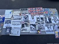 Wide view showing all photos, cards, and memorabilia arranged on a black surface including vintage black-and-white photos, team photos, and various baseball cards