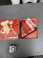 Top-down view of the barbecue gong and parts inside the original box along with a measuring tape for scale.