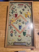 Full view of the vintage pinball game showing its wooden frame, baseball diamond playfield, colorful scoring targets, metal hooks, and cartoon baseball player graphics.