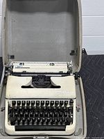 Front view of cream Olympia travel typewriter inside open hard carrying case on black padding.