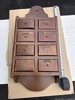 Full view of wooden spice cabinet with 8 drawers, showing size scale with measuring tape.