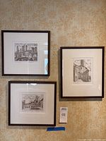 Three dark wood framed lithographs with white mats hung on patterned wall.