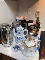 Full shot showing the four coffee makers, kettles including Sunbeam electric percolator, stove top Bialetti espresso maker, copper bottomed Revere Ware kettle, and ceramic teapots.